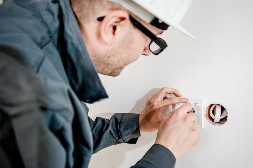 An electrician in a hard hat wiring a wall outlet