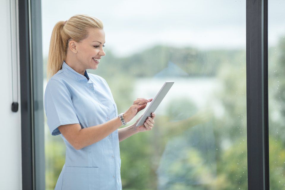 A health care worker in scrubs checking a tablet